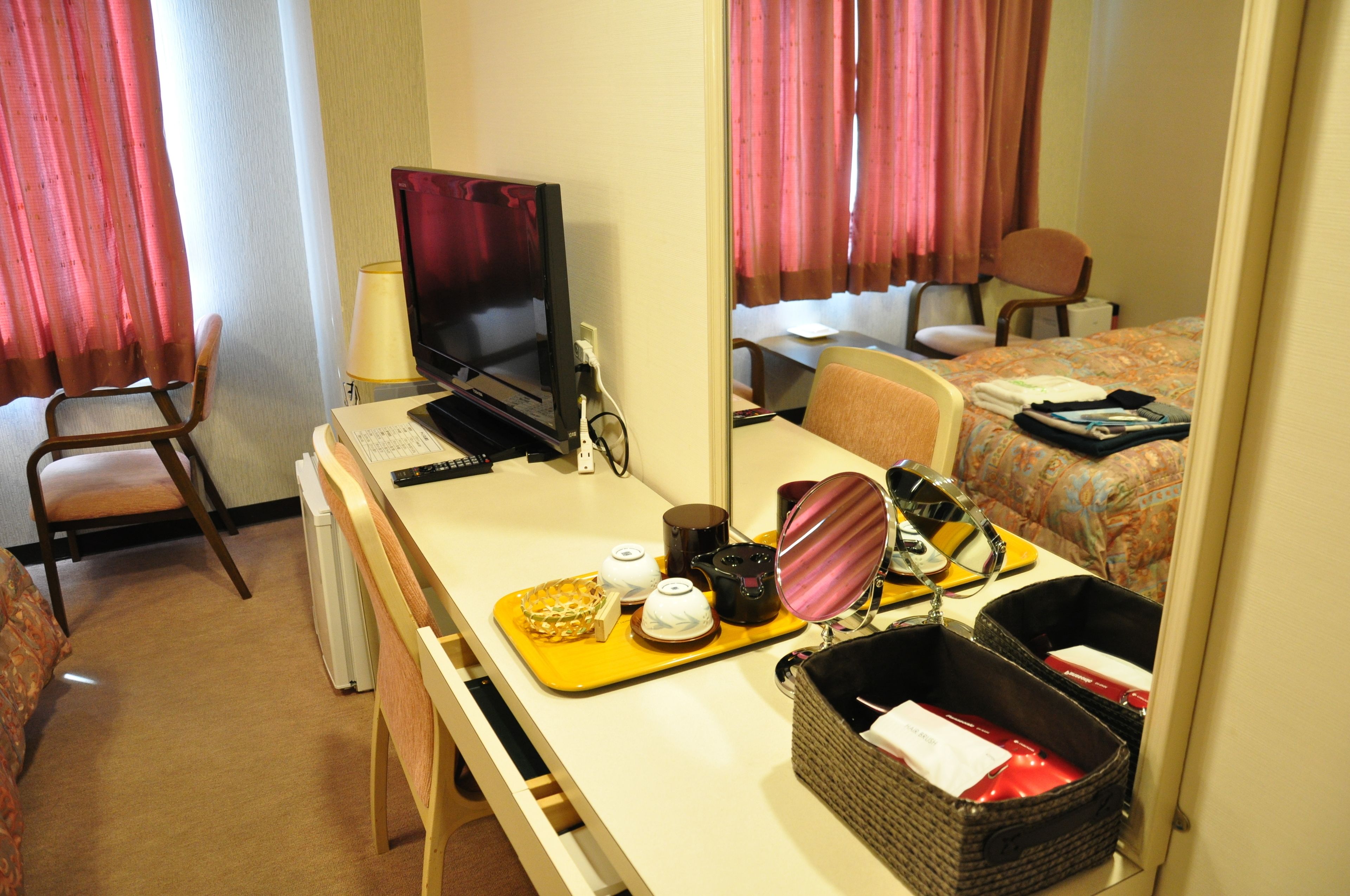 Ein Hotelzimmer mit Schreibtisch, Fernseher, Stuhl, Bett und Spiegel.