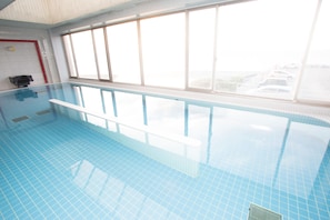 An indoor swimming pool with clear blue tiles, a white pool edge, and a window overlooking a parking area. - Kur & Hotel Suruga (Shizuoka)