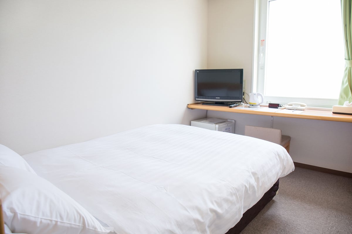 A hotel room with a bed, a desk with a laptop, a telephone, and a window with curtains.