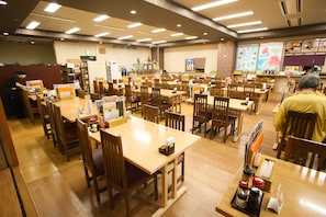 A spacious dining area with multiple wooden tables and chairs, a service counter, and a menu display on the wall. - Kur & Hotel Suruga (Shizuoka)