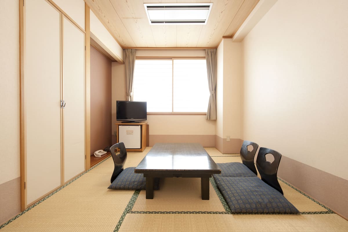A traditional Japanese room with tatami flooring, a low table, and a television on a cabinet.