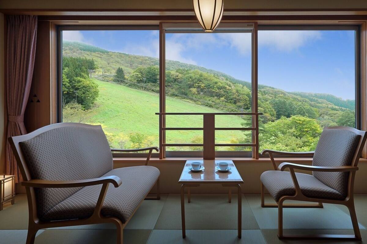 Una habitación con dos sillas, una mesa y vistas a un paisaje verde a través de ventanas amplias.