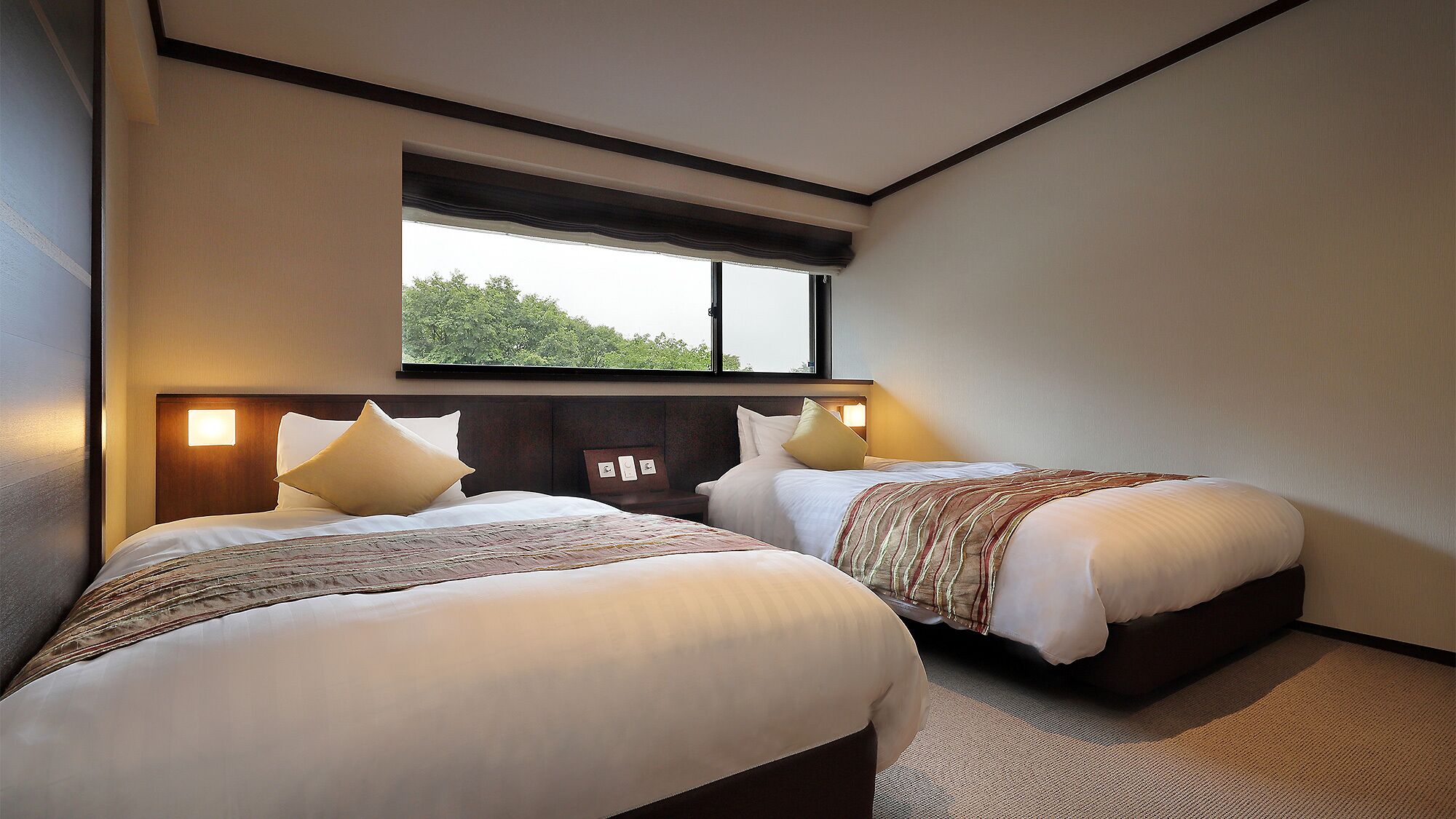 A hotel room with two beds, a large window, and a view of trees.