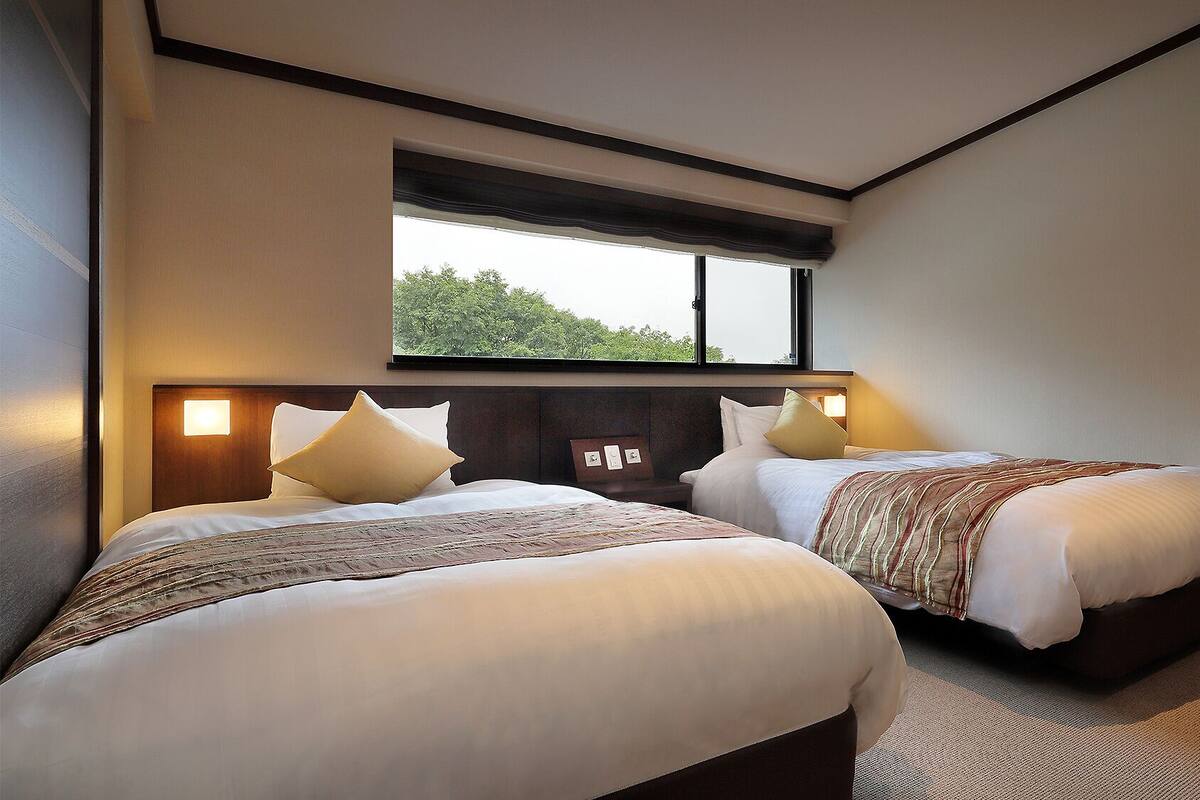 Una habitación de hotel con dos camas, un ventanal grande y vista a árboles.