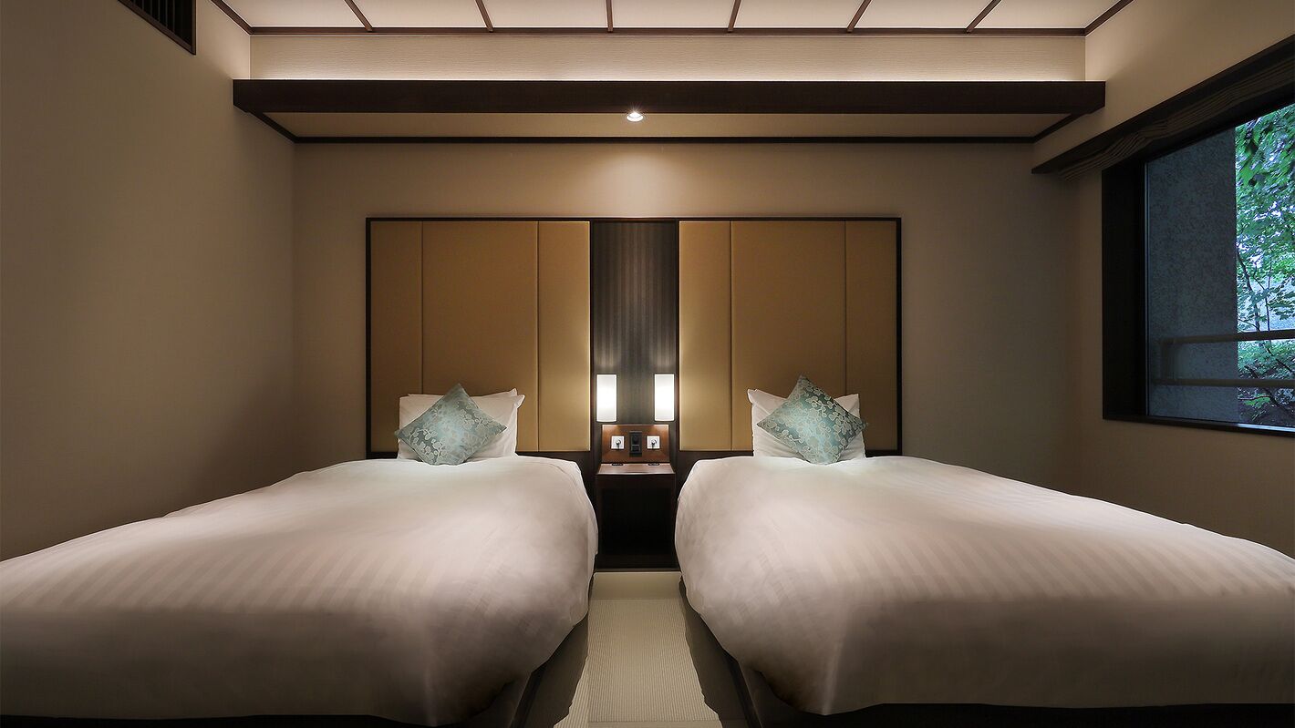 Habitación de hotel con dos camas, un espejo grande y una ventana con vistas a zonas verdes.