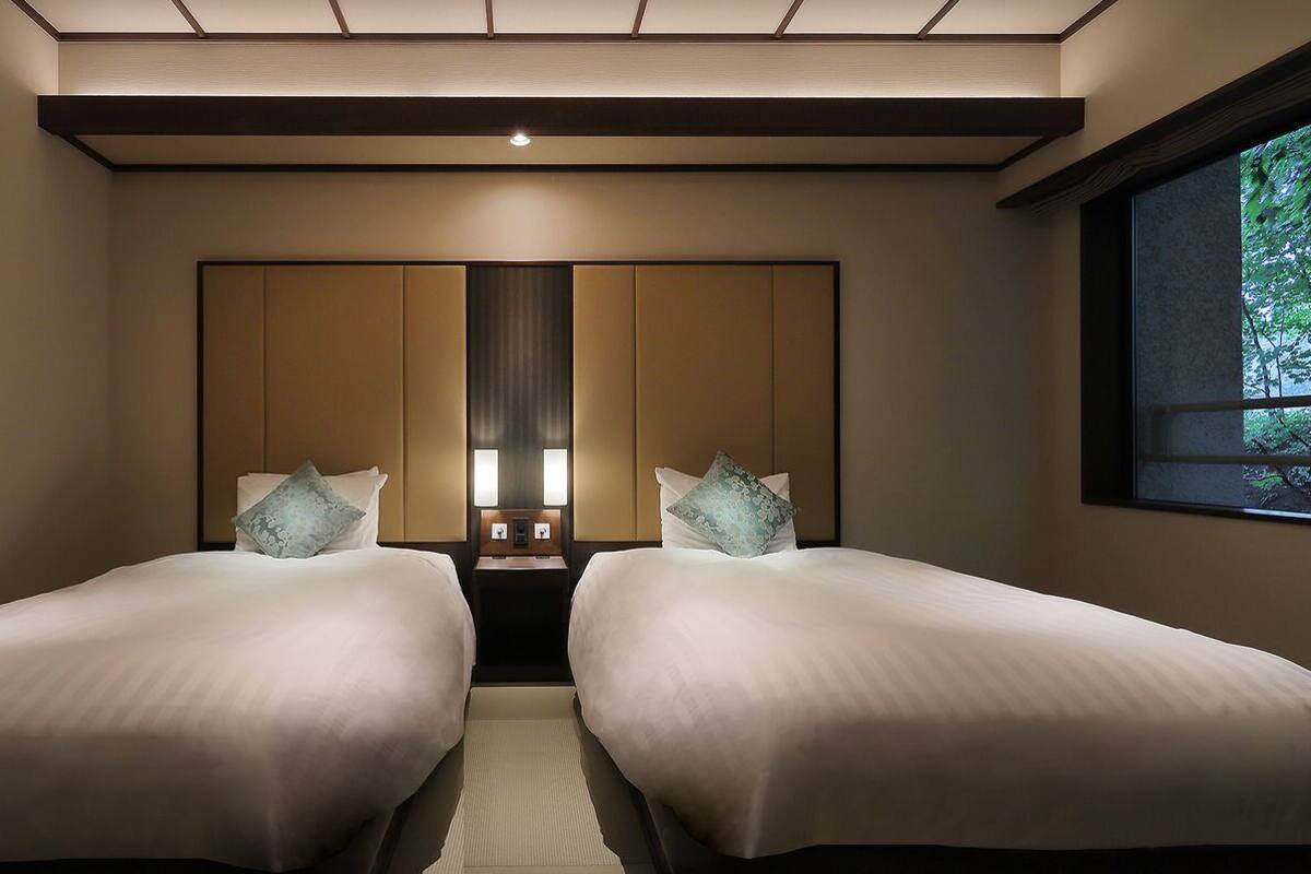 Habitación de hotel con dos camas, un espejo grande y una ventana con vistas a zonas verdes.