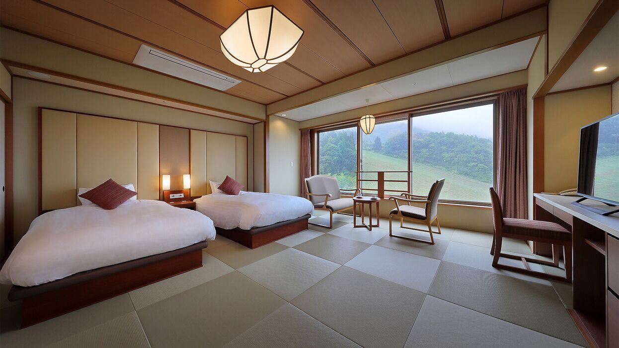 A hotel room with two beds, a desk, a chair, a TV, and a large window with a view of greenery.