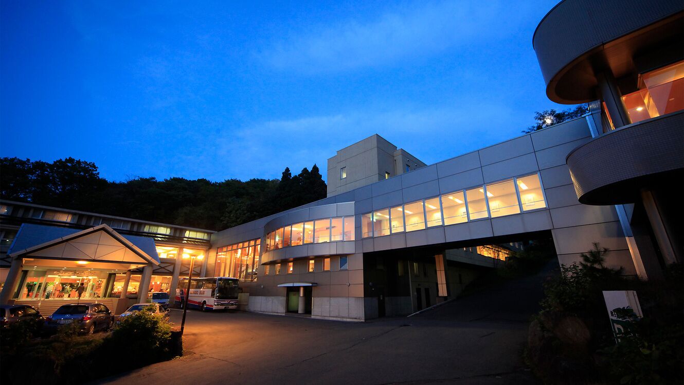 A modern building with a curved facade, large windows, and a covered entrance area.