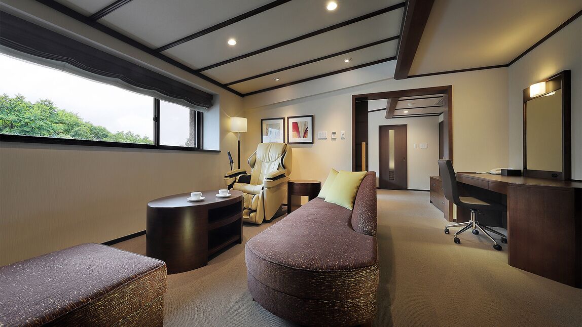 A modern hotel room with a large window, a sofa, a desk, a chair, and a small table.