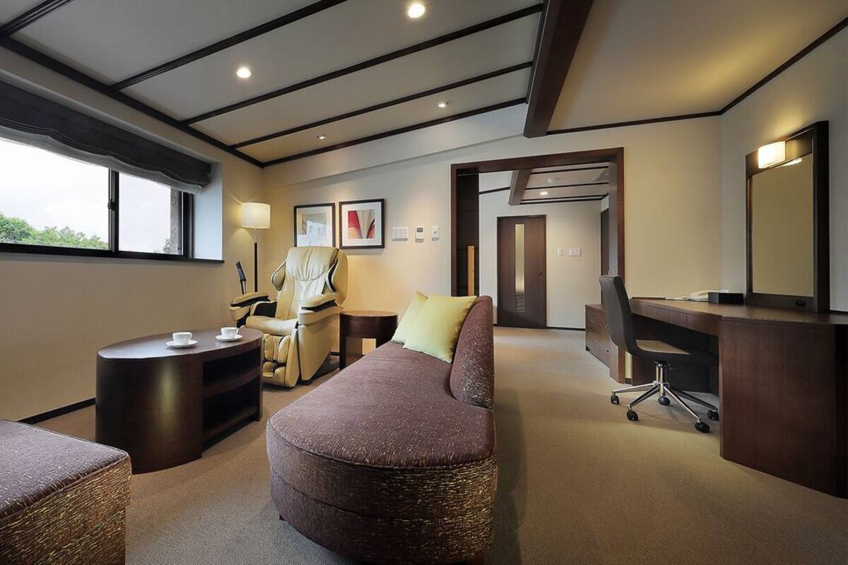 Una habitación de hotel moderna con un ventanal grande, un sofá, un escritorio, una silla y una mesita.
