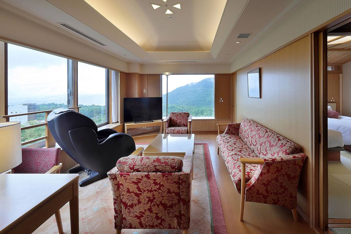 Una habitación de hotel con un ventanal grande, un sofá, una silla, un televisor y una cama.