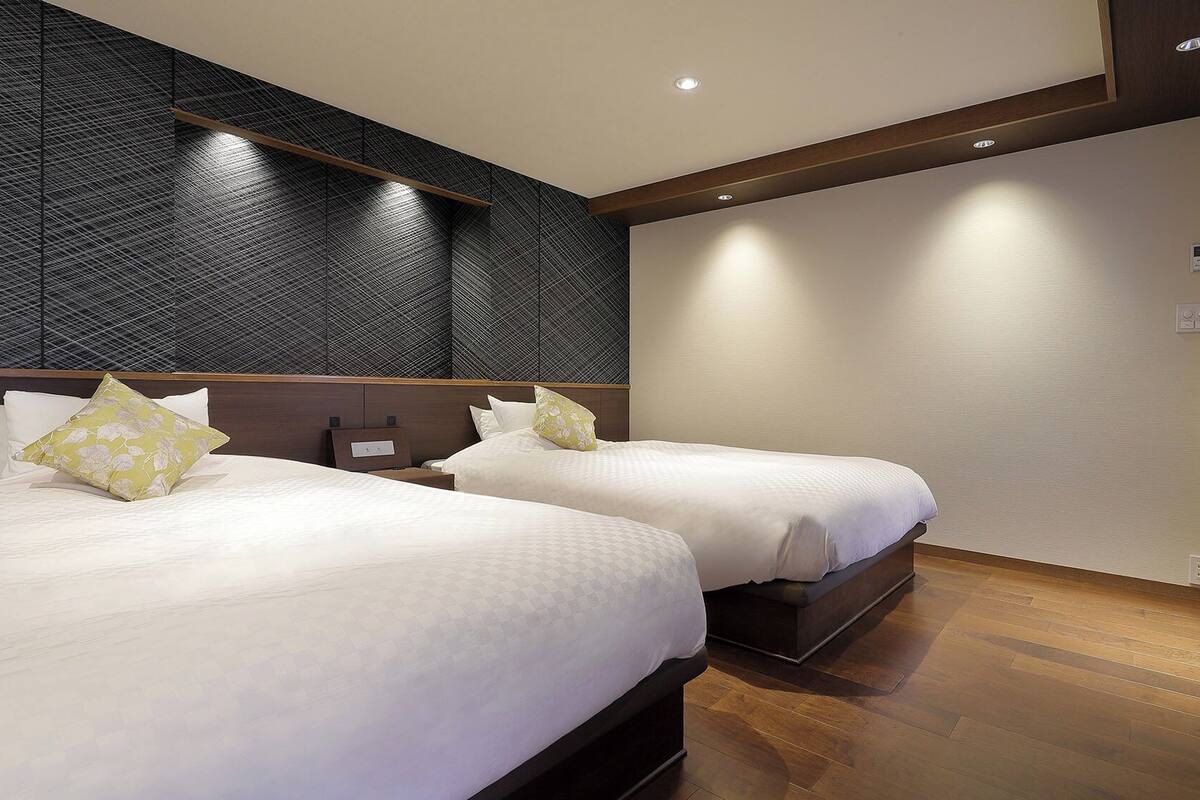 Habitación de hotel con dos camas, pared oscura con textura y suelo de madera.