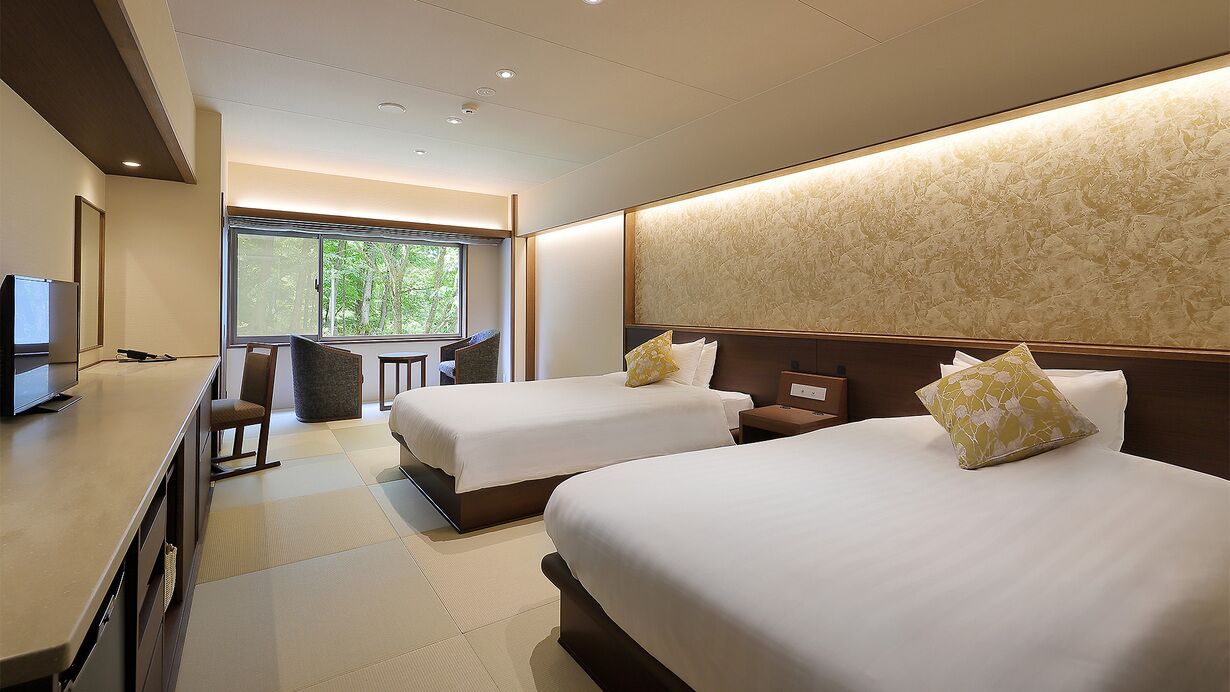 A hotel room with two beds, a desk, a chair, and a large window.