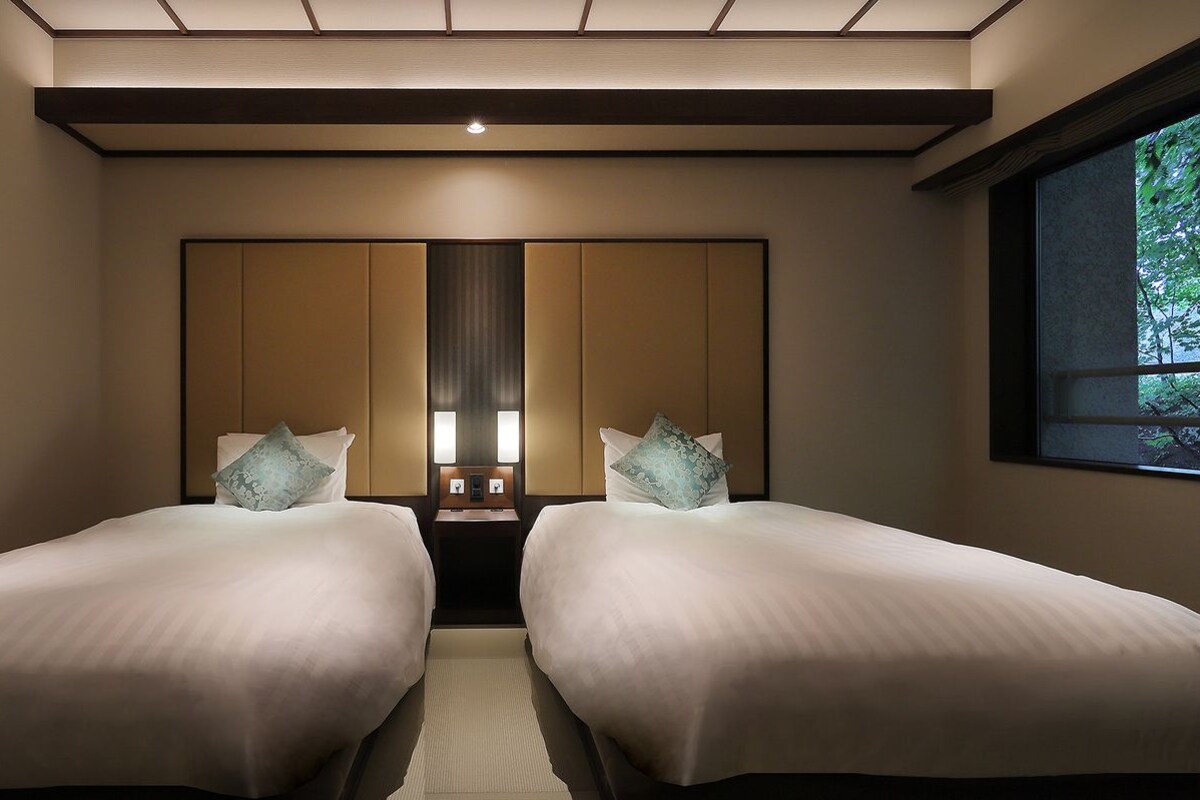 Habitación de hotel con dos camas, un espejo grande y una ventana con vistas a zonas verdes.