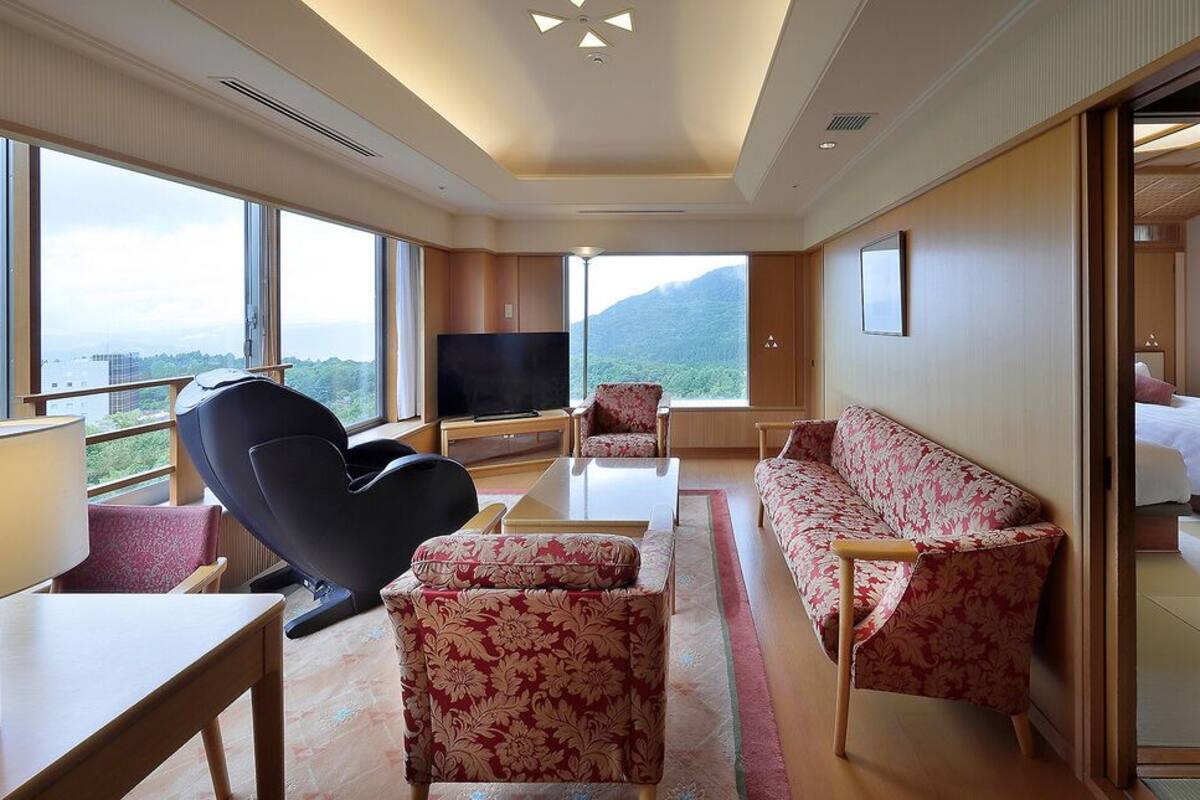 Habitación de hotel con sofá, sillón, televisión y cama.