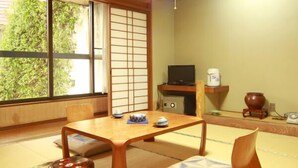 Perinteinen japanilainen huone, jossa on tatamimatto, matala pöytä, televisio ja näkymä vehreään maisemaan.