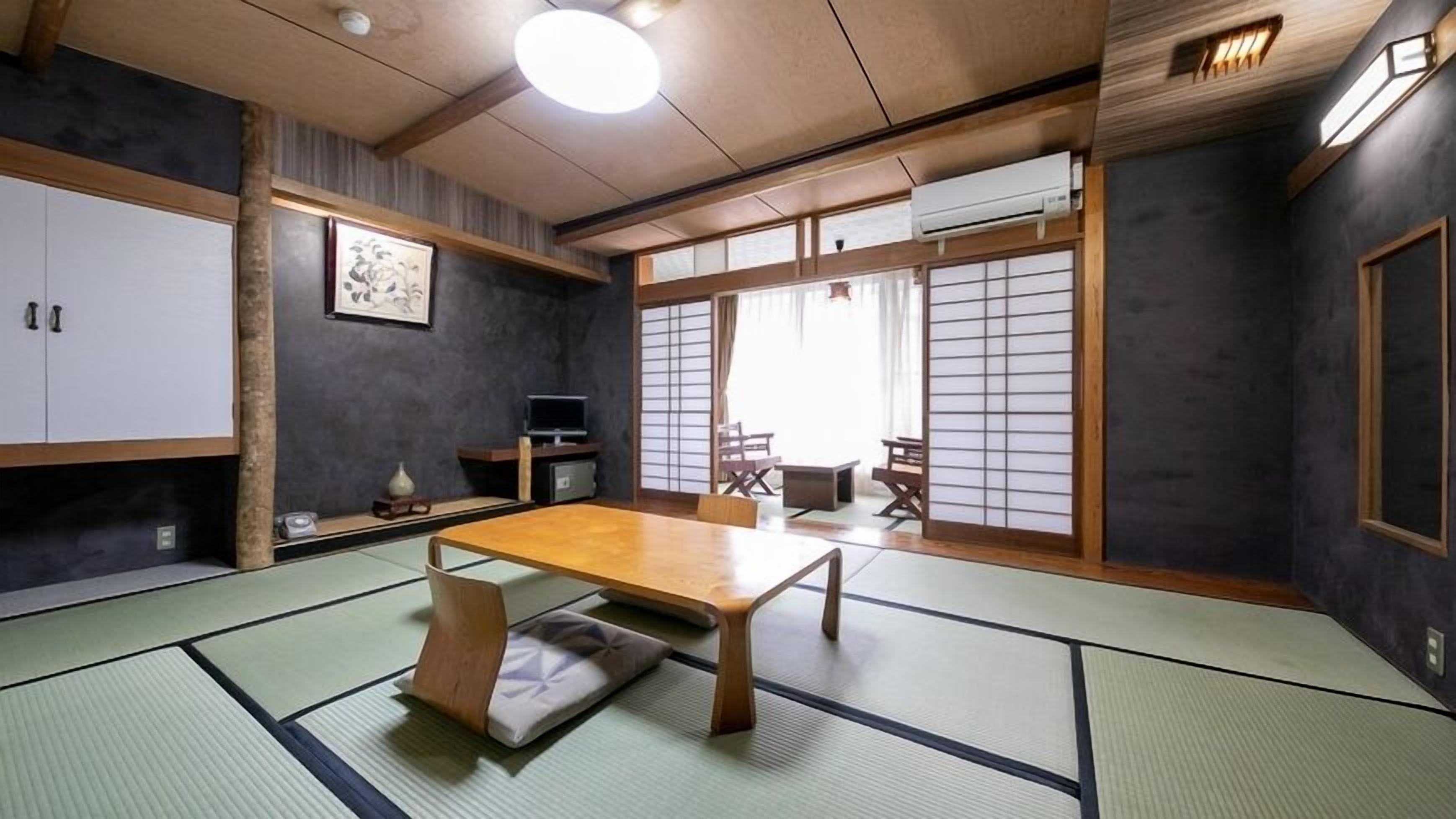 A traditional Japanese room with tatami flooring, a low table, sliding doors, and a television.