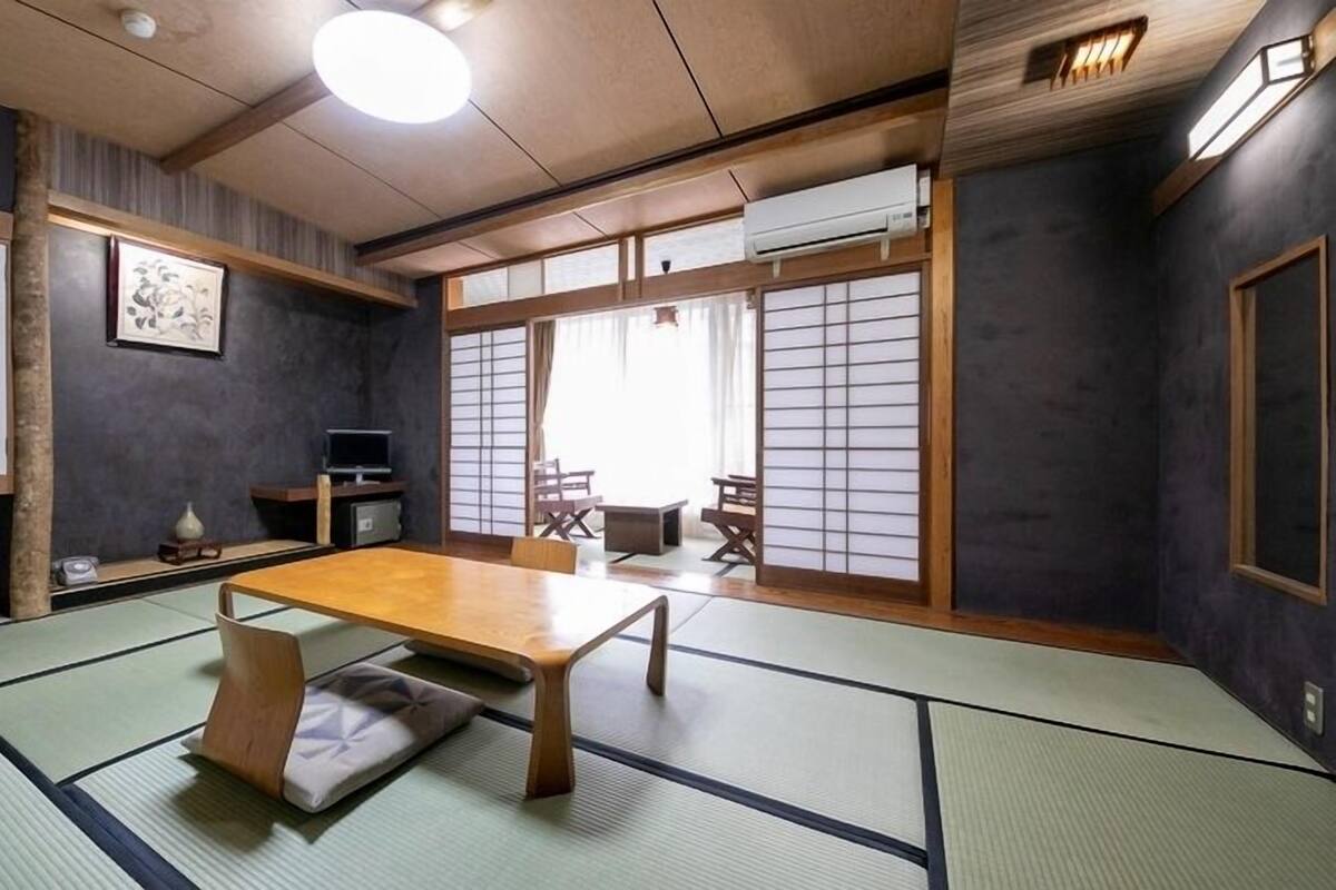 A traditional Japanese room with tatami flooring, a low table, sliding doors, and a television.