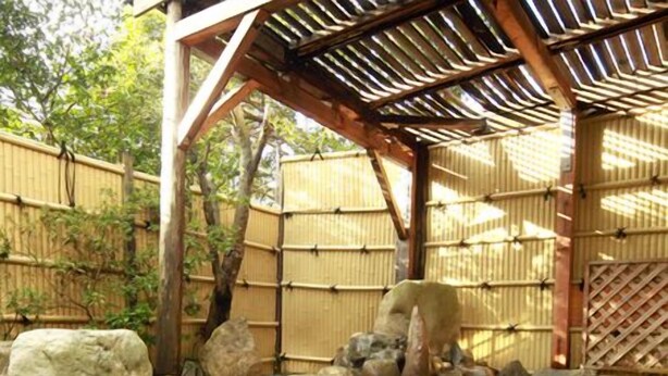 Perinteinen japanilainen onsen-kylpylä, jossa on puinen rakenne, bambuseinät ja kivipolku, joka johtaa veteen.