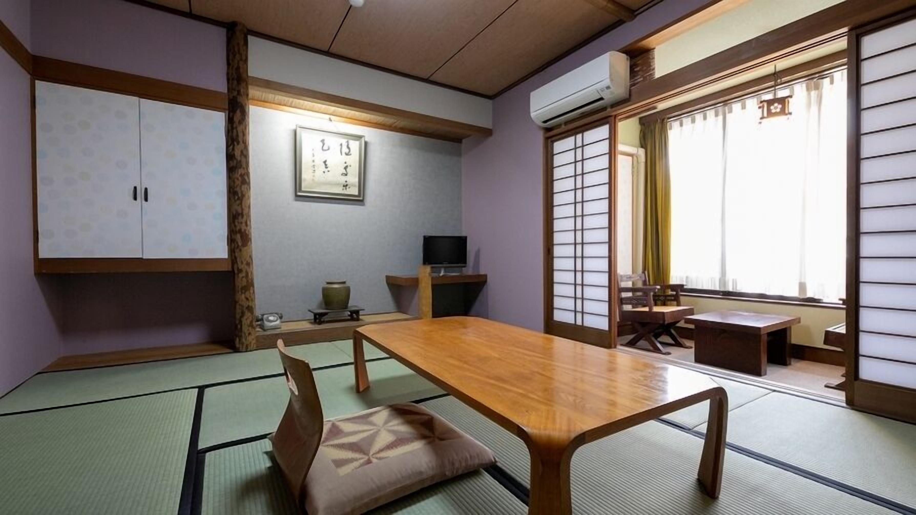 A traditional Japanese room with tatami flooring, a low table, a TV, and sliding doors.