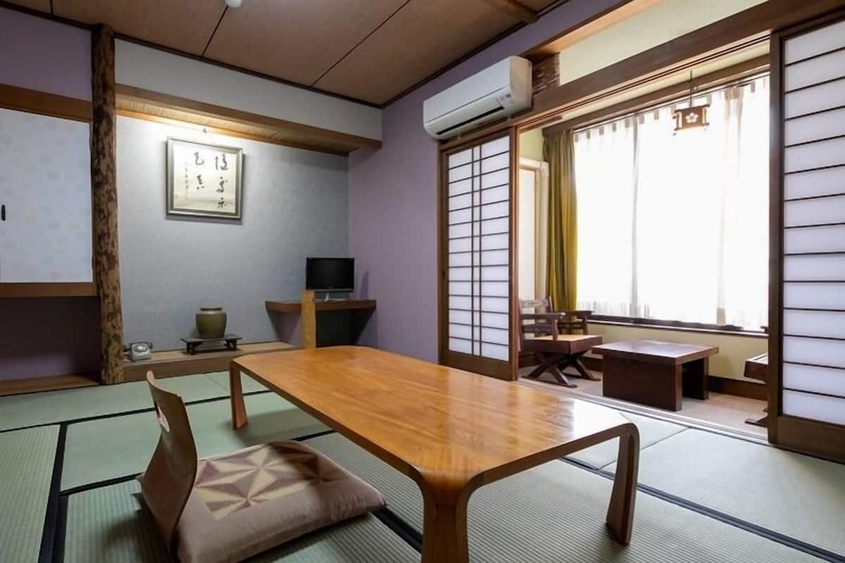 A traditional Japanese room with tatami flooring, a low table, a TV, and sliding doors.