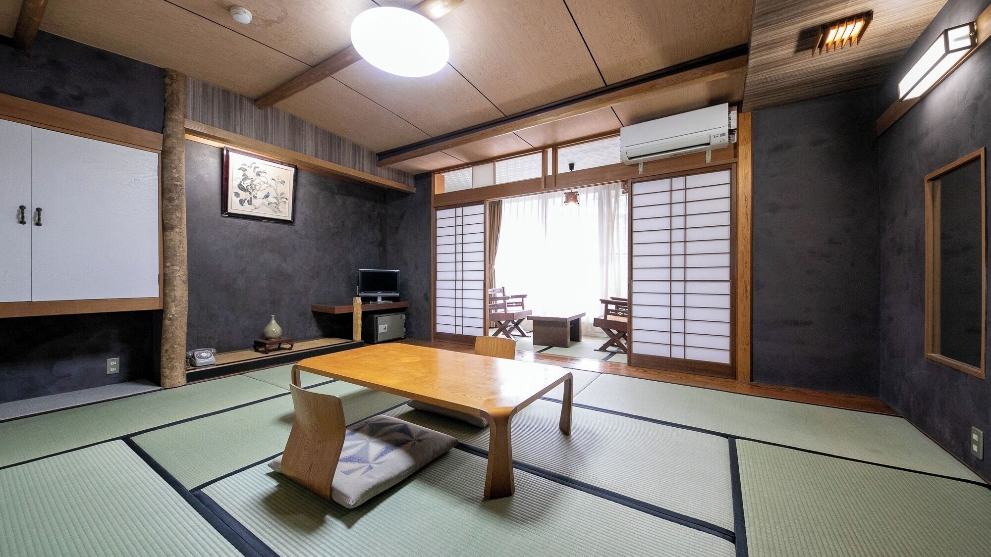 Une pièce de style japonais traditionnel, avec un sol recouvert de tatamis, une table basse, des portes coulissantes et un téléviseur.