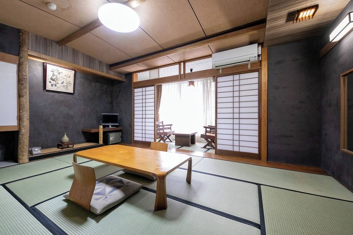 A traditional Japanese room with tatami flooring, a low table, sliding doors, and a television.