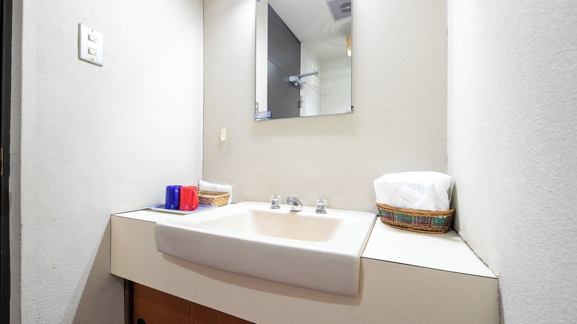 Une salle de bain avec un lavabo blanc, un miroir et un panier contenant une serviette.