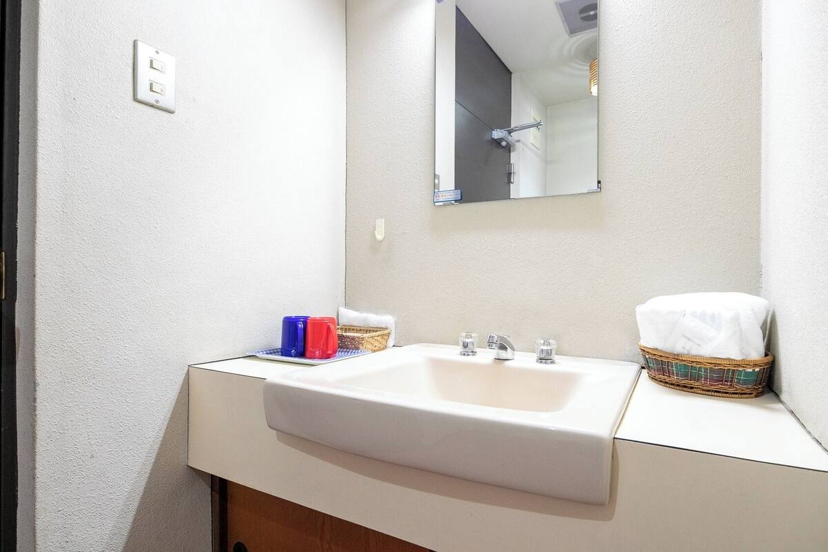 A bathroom with a white sink, a mirror, and a basket with a towel.