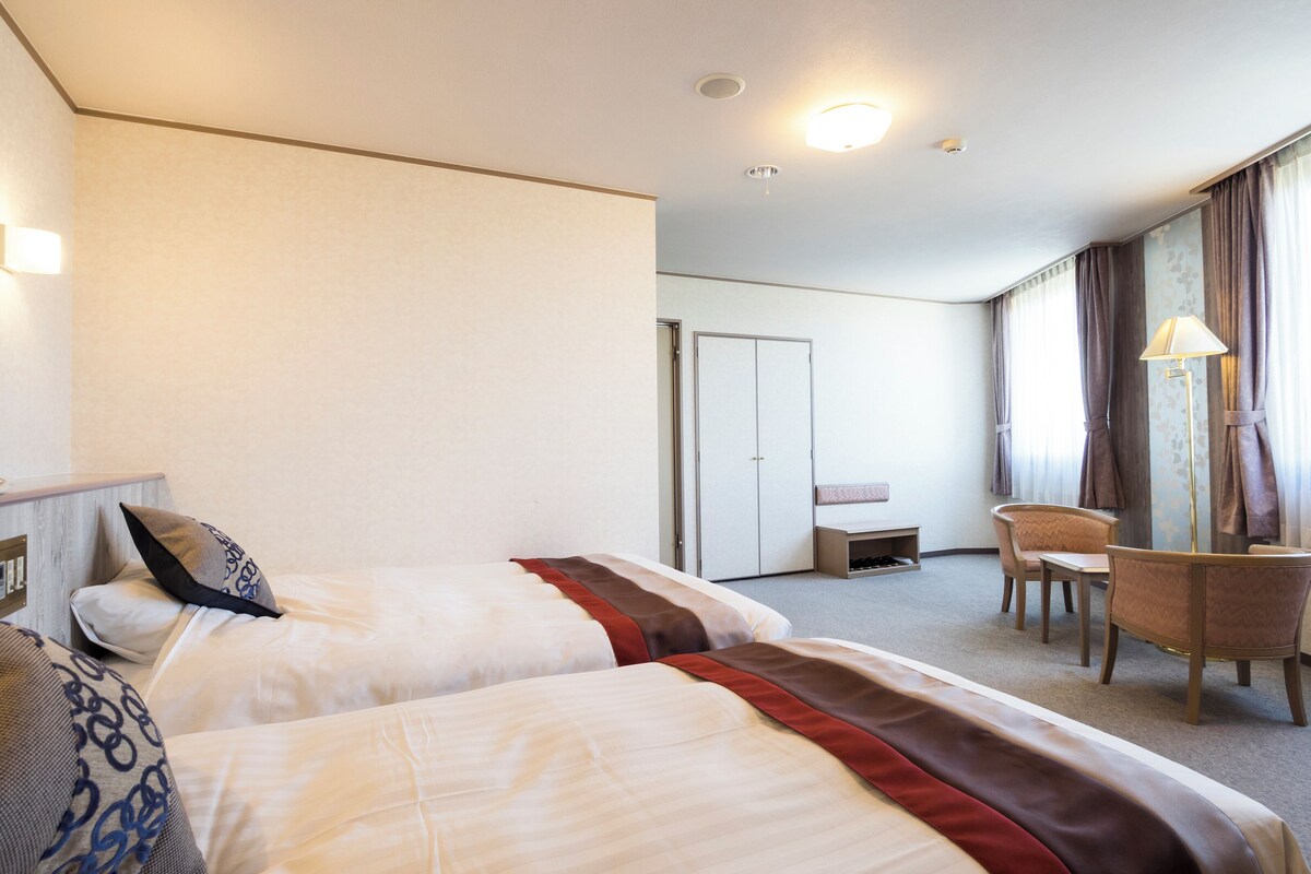A hotel room with two beds, a desk, a chair, and a wardrobe.
