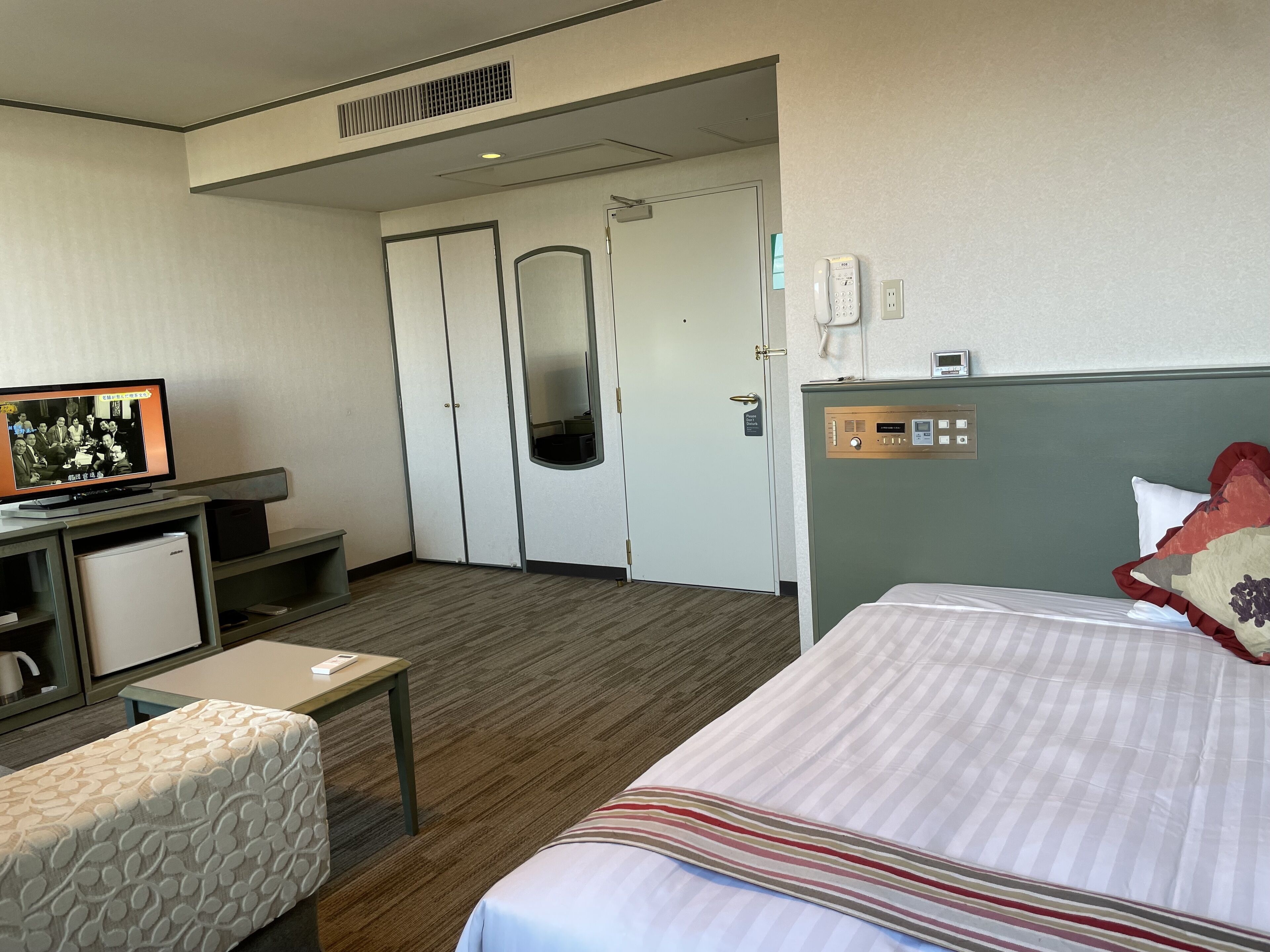 Una habitación de hotel con cama, escritorio con computadora, televisor, refrigerador pequeño y puerta que da a otra habitación.
