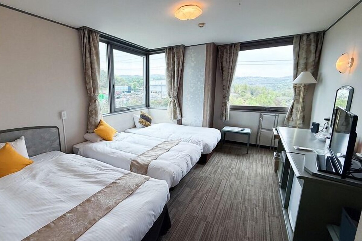 A hotel room with two beds, a desk, a chair, and a computer.