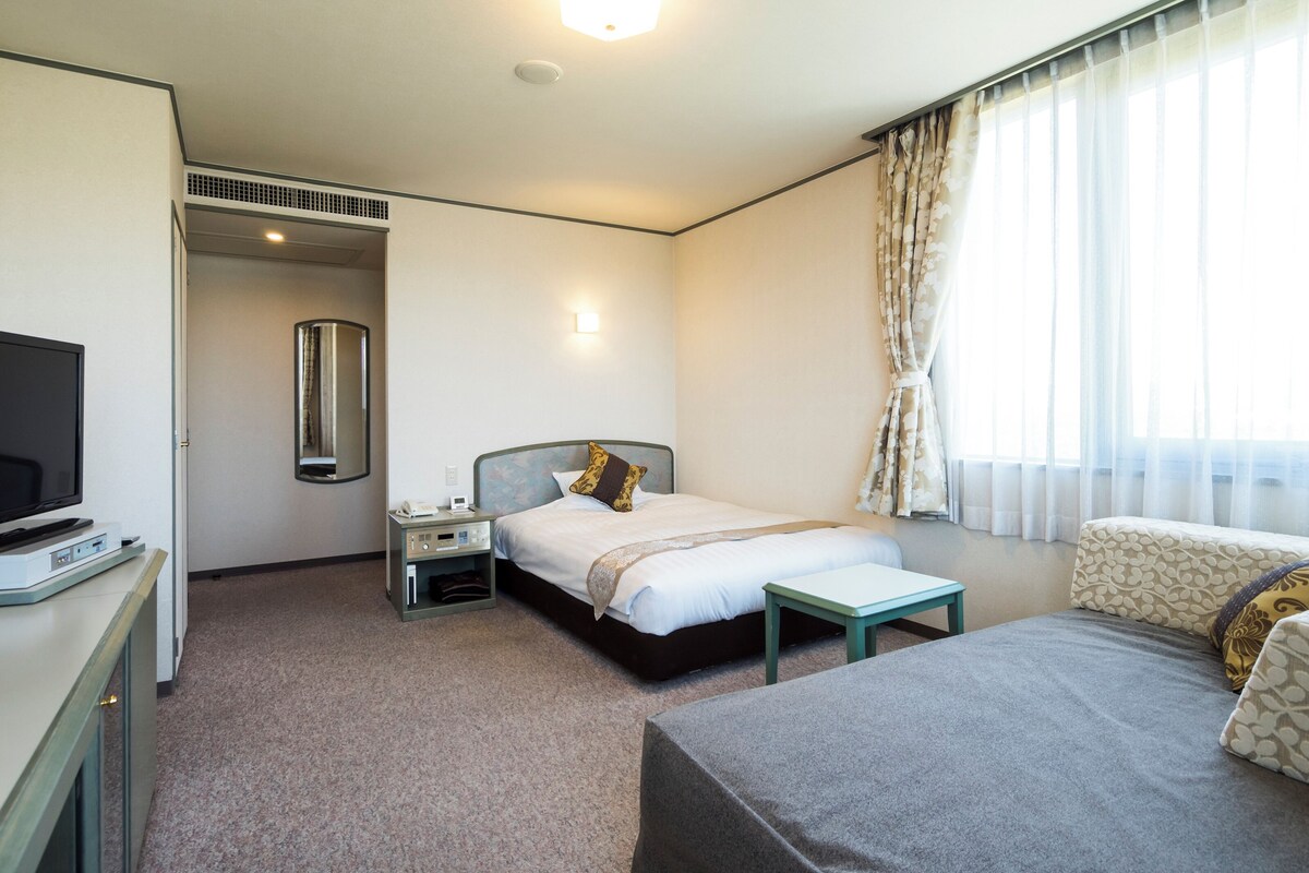A hotel room with a bed, bedside table, TV, and a desk with a computer.