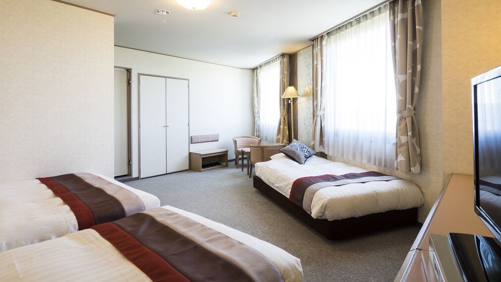 A hotel room with two beds, a desk, a chair, a TV, and a wardrobe.