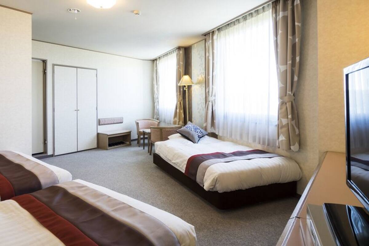 A hotel room with two beds, a desk, a chair, a TV, and a wardrobe.