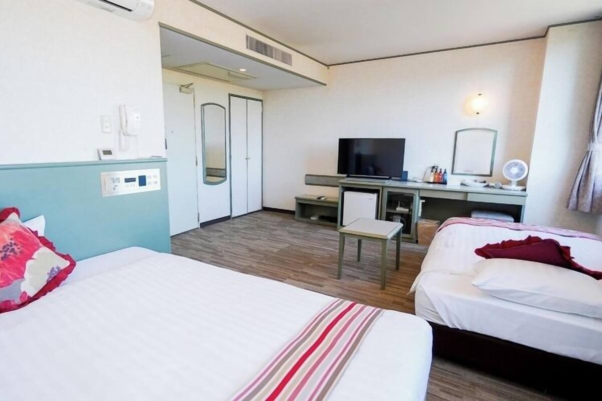 A hotel room with two beds, a desk with a TV, a chair, and a small table.