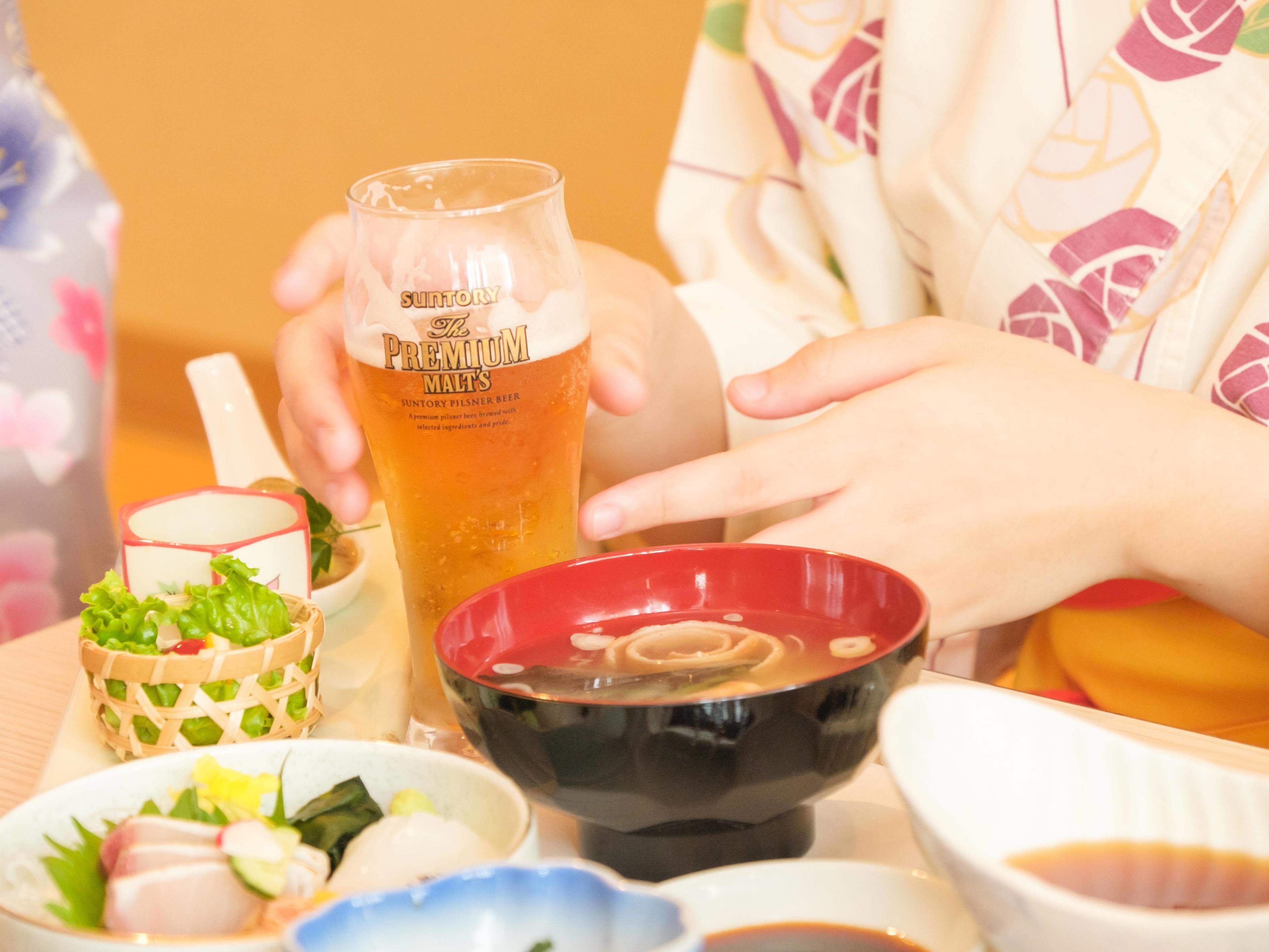 Een tafel met diverse gerechten, waaronder een kom soep, een bord sashimi en een glas bier.