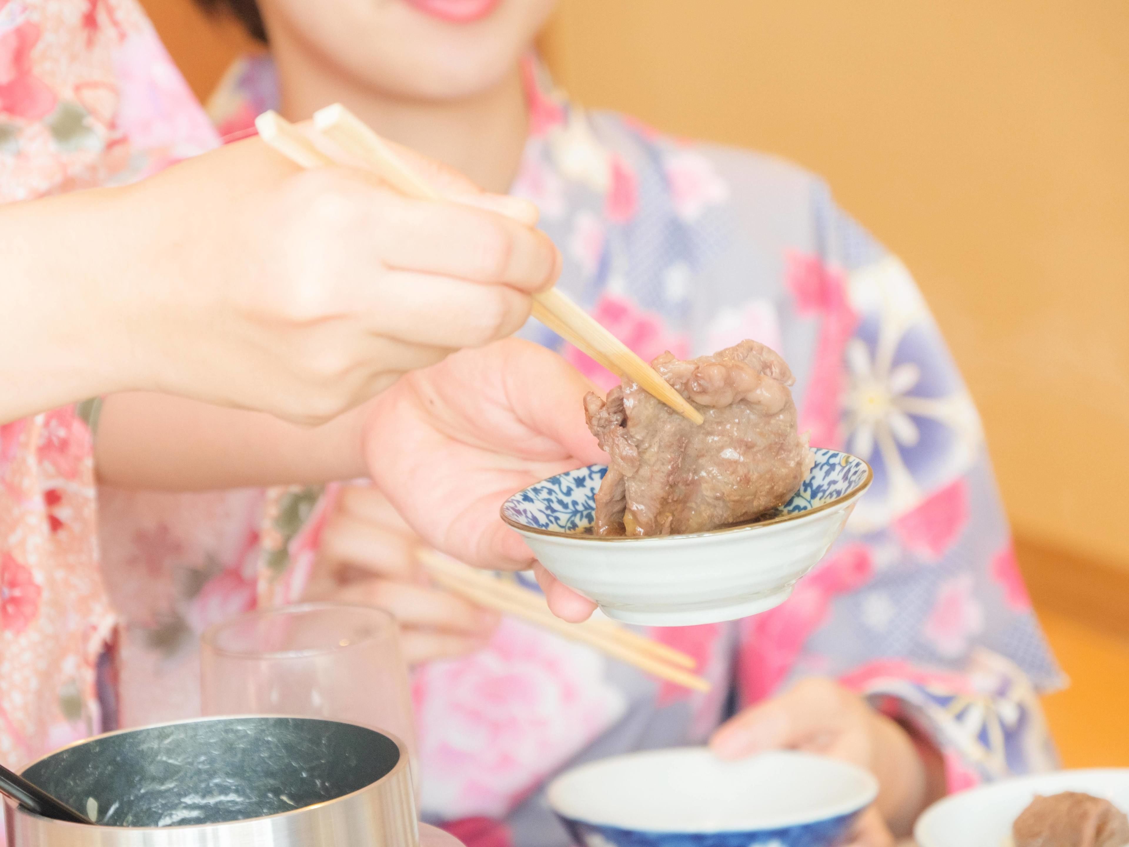 A person holding a bowl with chopsticks, a pot, and a cup on a table.