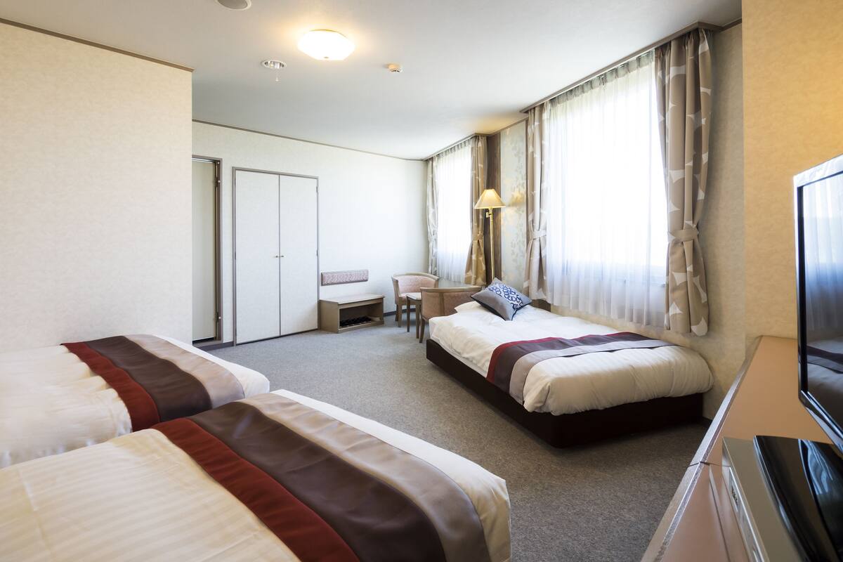 A hotel room with two beds, a desk, a chair, a TV, and a wardrobe.