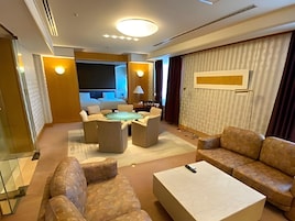 A modern hotel room with a seating area, a flat-screen TV, and a large window.