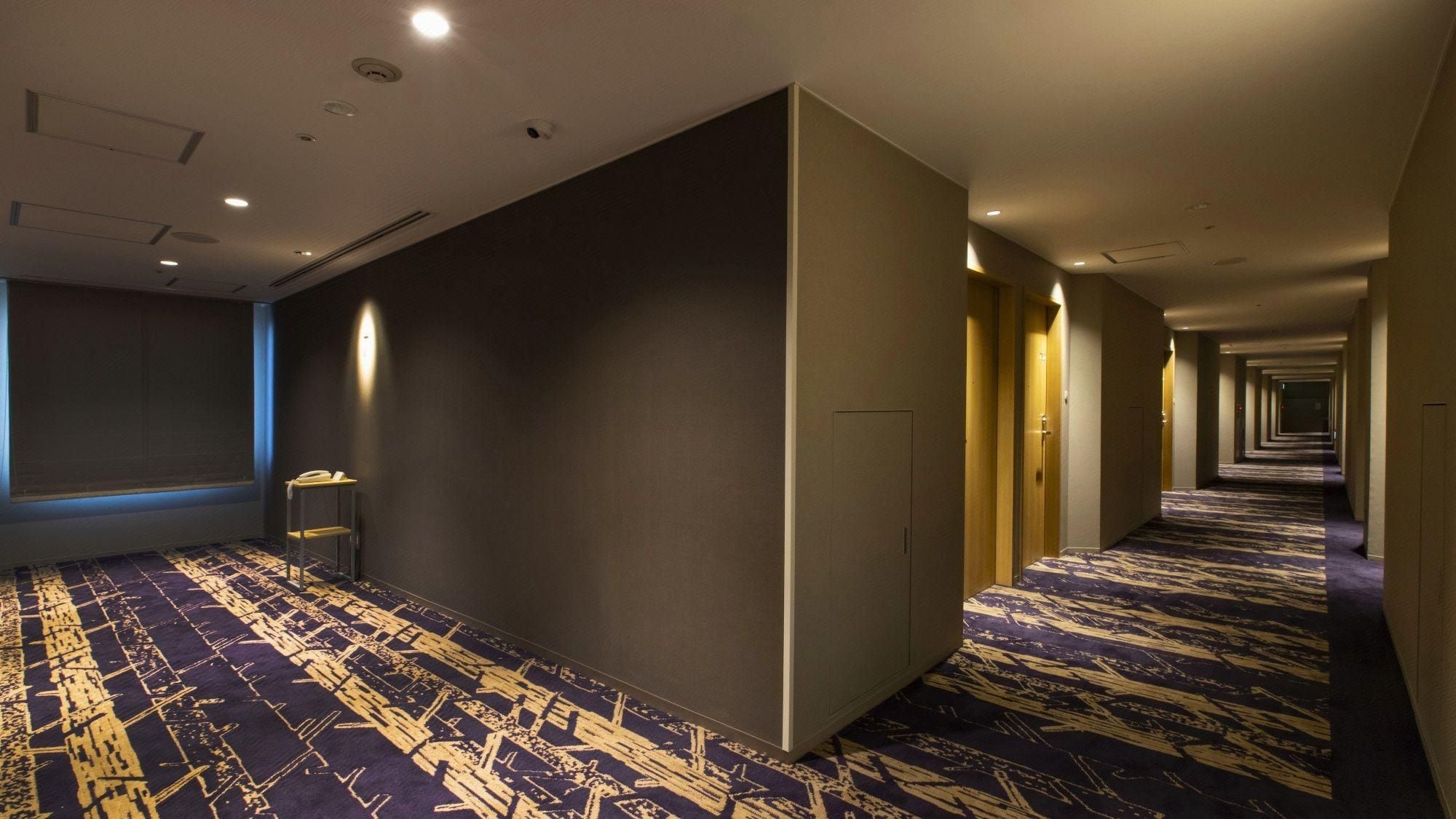 Un corridoio di hotel con tappeto a motivi, un telefono su supporto e porte che conducono alle camere.
