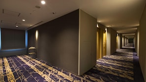 Un pasillo de hotel con alfombra estampada, un teléfono en un soporte y puertas que dan a habitaciones.
