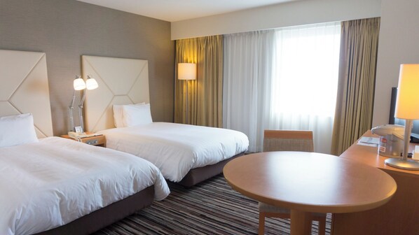 A hotel room with two beds, a round table, a lamp, and a window with curtains.