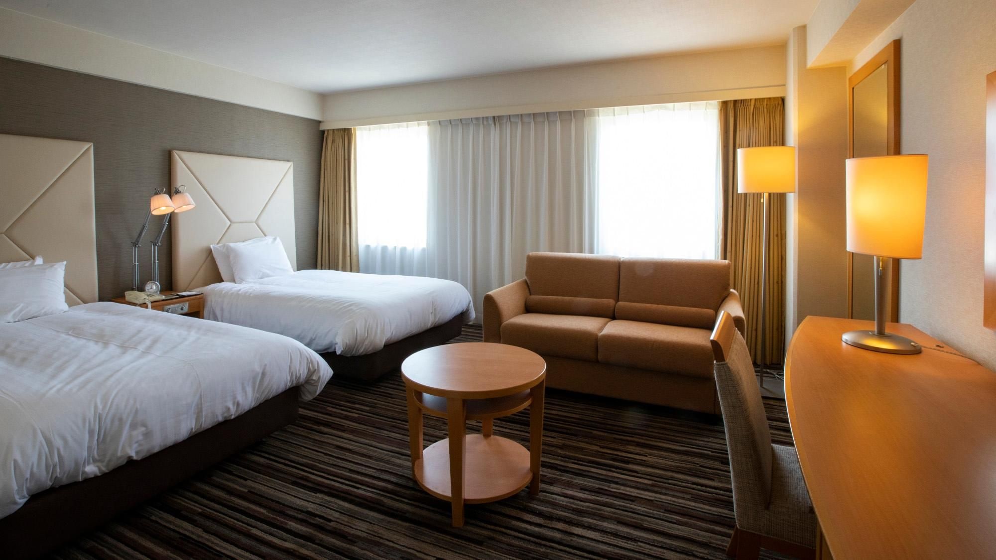 A hotel room with two beds, a sofa, a round table, and a lamp.
