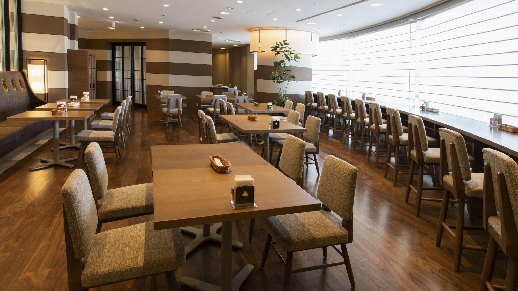 Un espace de restauration moderne, doté de plusieurs tables et chaises, d’un plancher en bois et d’une grande fenêtre laissant entrer la lumière naturelle.