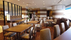 Moderni ravintola, jossa on raidalliset seinät, puupöydät ja pehmustetut tuolit.