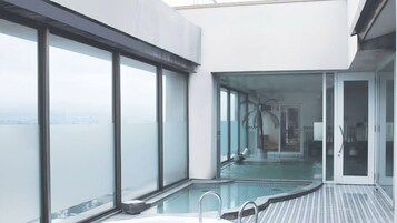 Una piscina interior moderna con paredes de vidrio, vistas despejadas del paisaje urbano y suelo de baldosas.
