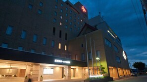 A hotel with multiple floors, a prominent red logo on the top, and a well-lit entrance area. - Tokyo Dai-ichi Hotel Tsuruoka (Tsuruoka)