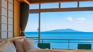 Habitación de hotel con un gran ventanal que ofrece vista al mar y una montaña distante.