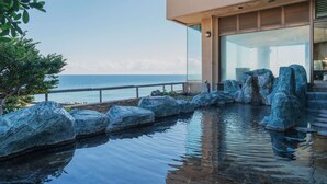 Un edificio moderno con piscina, rocas grandes y vista al océano.